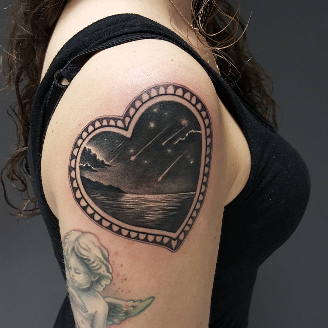 heart shaped frame and seashore and falling stars inside it. Tattoo on shoulder