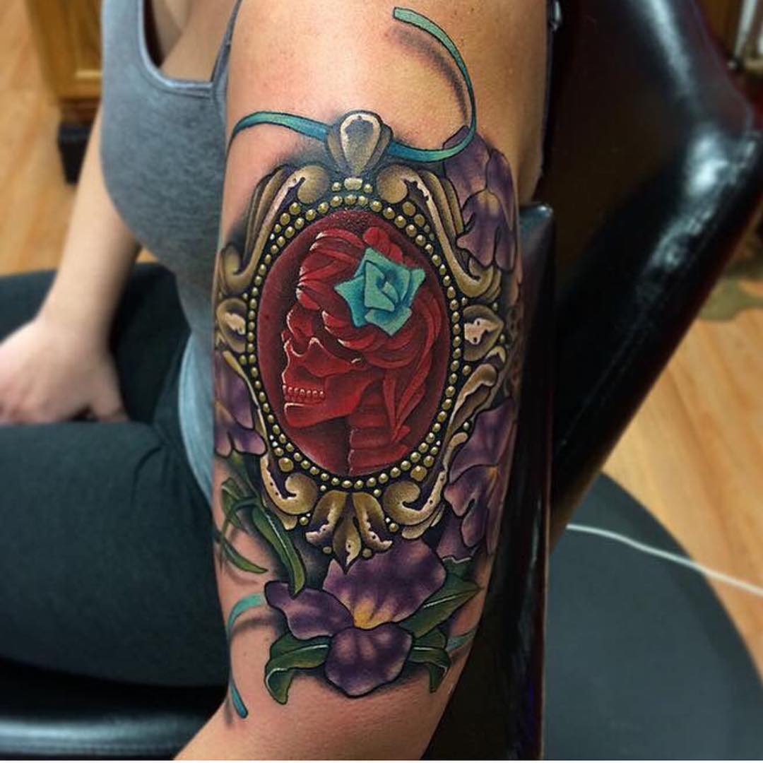 a tattoo placed on shoulder - ornamental locket medallion with a red skull inside it