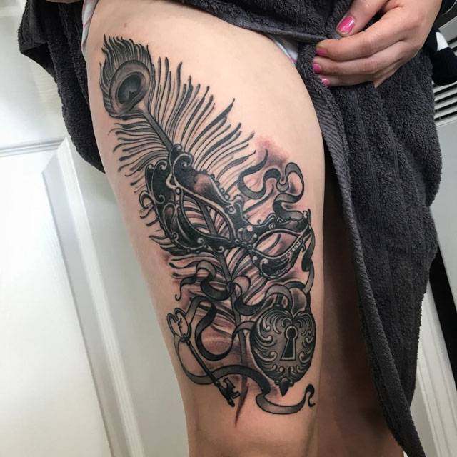 feather lock and masquerade mask tattoo on thigh